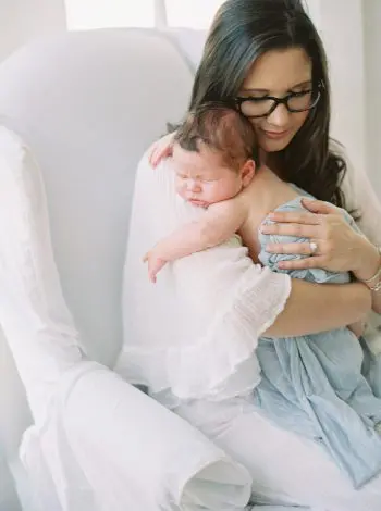 Portrait Mom embracing newborn baby boy in wingback chair at Katrina Barrow Photography Studio