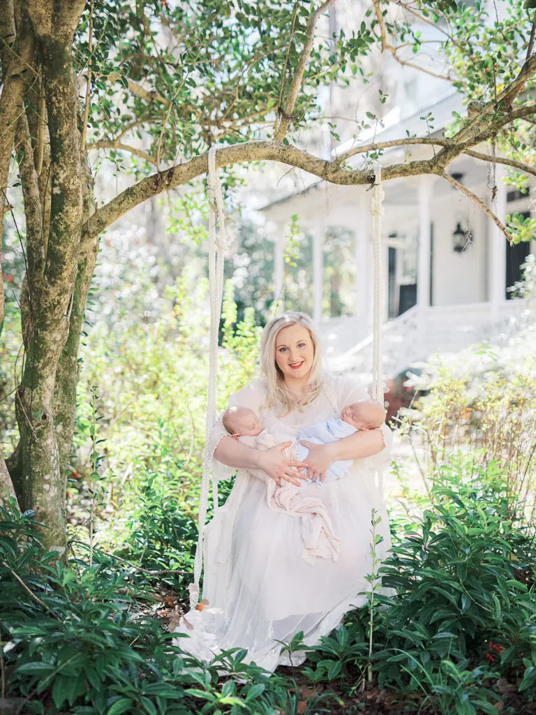 Portrait of a Mom holding newborn boy girl twins on a swing outside