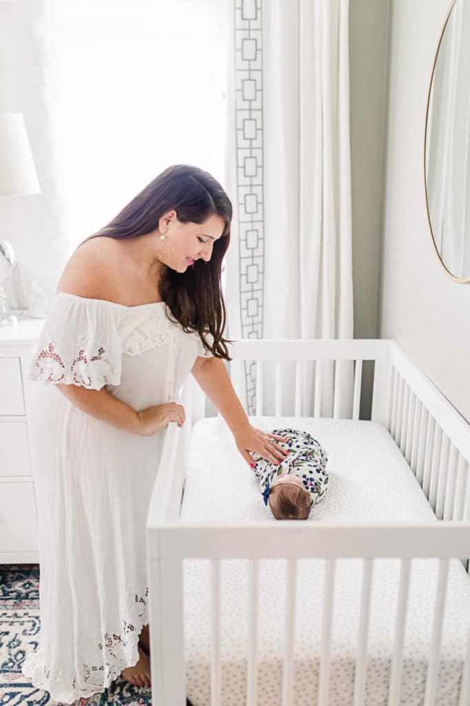Picture of mom tucking newborn baby girl to bed in white crib