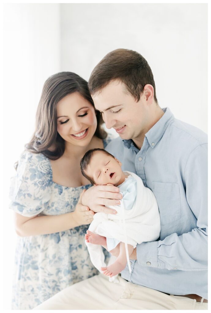 Mom wearing a blue and white dress holding her new baby with her husband in a Savannah Ga Newborn Photographer Studio